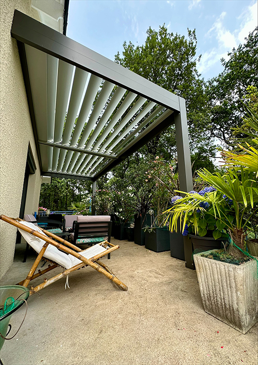 Lames orientables d'une pergola bioclimatique en aluminium anthracite sur terrasse avec salon de jardin, posée par Clin Menuiserie