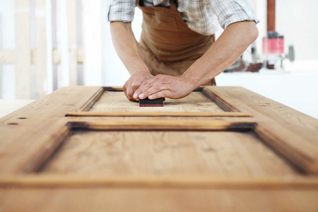 Artisan ponçant le panneau d'une porte en bois lors de son entretien